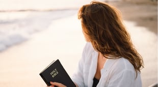 Woman reading bible on beach at sunrise