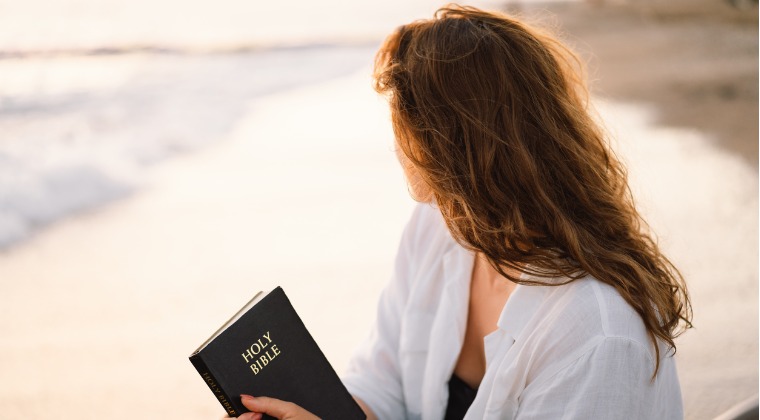 Woman reading bible on beach at sunrise