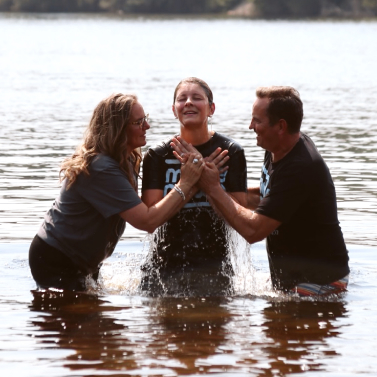 two people baptizing young woman in lake
