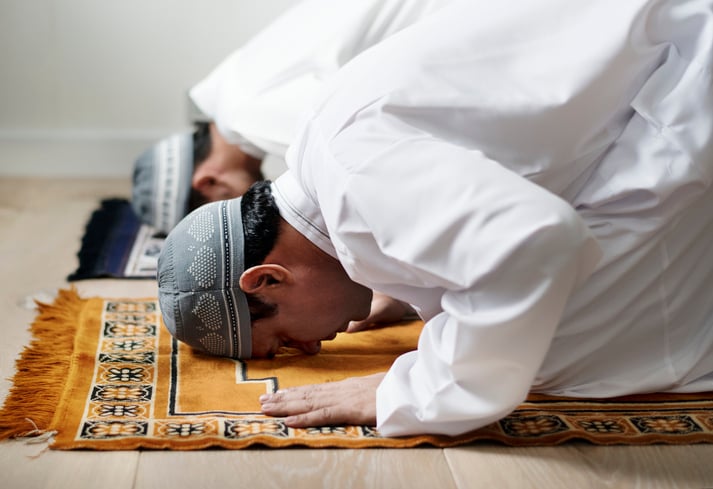 Two men praying on mats in traditional Islamic sujood position