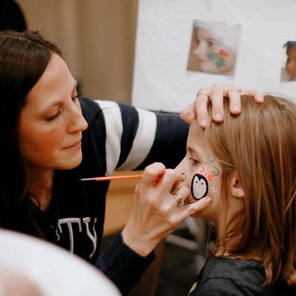 adult putting face painting of a penguin on child face