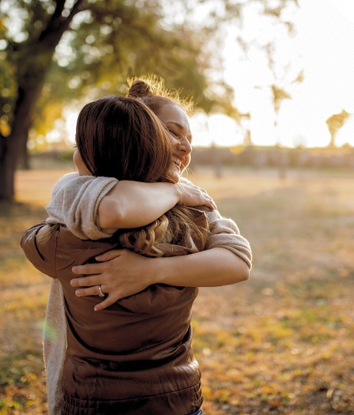 two women hugging in front of sunset