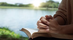 hands resting on bible in prayer with lake in background