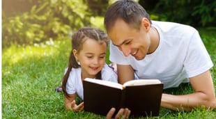 father reading bible to daughter in the grass